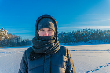 Fototapeta na wymiar Portrait of a woman standing on frozen lake on a frosty sunny day against the background of a forest