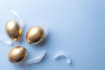Easter eggs Golden color egg with white feathers on pastel blue background in Happy Easter decoration. Festive decoration in flat lay.