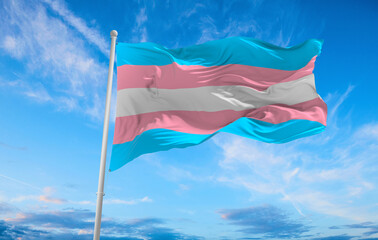flag of transgender Pride waving in the wind on flagpole against the sky with clouds on sunny day