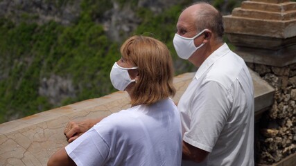 Senior couple in protective face masks enjoying the breathtaking view of the ocean from an observation deck . Traveling during covid-19 pandemic concept. 