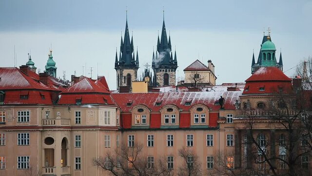 Evening Prague. Chimney smoke against black spiers of The Church of Mother of God before Tyn, seagulls fly by. Lights are on in the windows of the red-tiled building.
