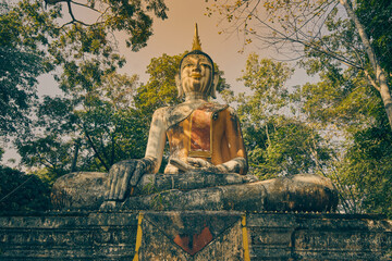 Phayao, Thailand - Dec 6, 2020: Low Angle Front Meditation Buddha Statue in Green Forest and Blue Sky Background in Wat Analayo Temple in Vintage Tone