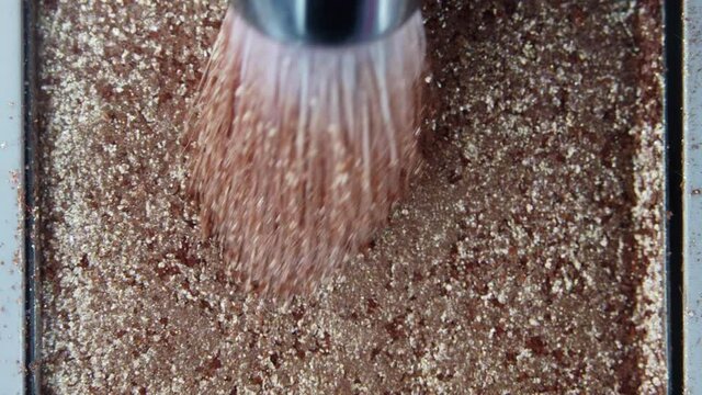 Macro view of makeup artist working with eyeshadow sparkle palette. Brush gains glitter on pile. Working process, tools in beauty industry. Advertising products, cosmetics concept.