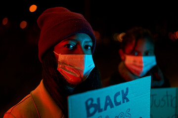 Close-up of an African-American girl holding a banner while standing in a crowd of protesters....