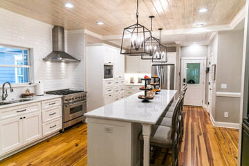 Large renovated white kitchen with textured subway tile, black iron lights and pine hardwood...