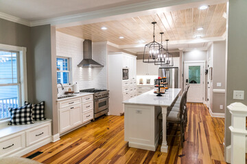 Large renovated white kitchen with textured subway tile, black iron lights and pine hardwood flooring