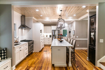 Large renovated white kitchen with textured subway tile, black iron lights and pine hardwood flooring
