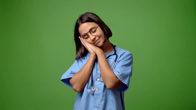 Woman with nurse uniform making sleep gesture. Adorable and sweet expression