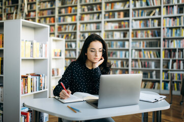 Concentrated caucasian woman sit at the desk, using laptop. Focused young adult female freelancer planning a business project, or studying online