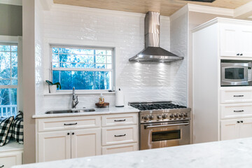Large renovated white kitchen with textured subway tile, black iron lights and pine hardwood flooring