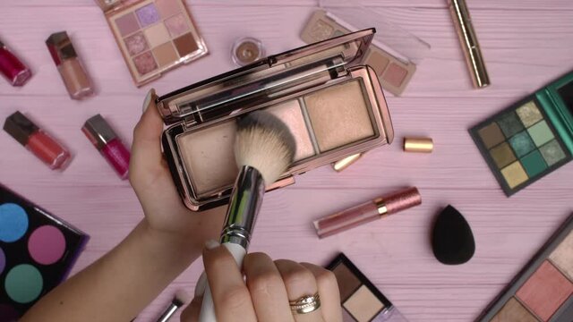 Woman working with face contouring palette - powder, bronzer and highlighter on pink flat lay cosmetics collection background. Tools in beauty industry - lipsticks, eyeshadows, glosses. 