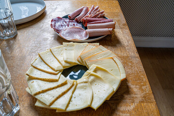 Detail photograph of a French raclette with all the typical ingredients, varieties of French cheeses, boiled potatoes, carrots, mushrooms, mushrooms, cucumbers and sausages, under natural light 