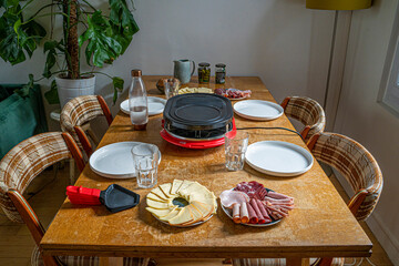 Detail photograph of a French raclette with all the typical ingredients, varieties of French cheeses, boiled potatoes, carrots, mushrooms, mushrooms, cucumbers and sausages, under natural light 