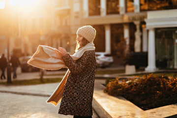 Obraz premium Graceful caucasian girl wears coat and scarf posing on the street. Merry woman in knitted hat chilling in autumn.