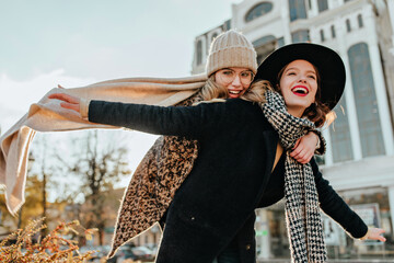 Spectacular woman in black coat expressing happiness. Inspired female friends fooling around on the street.