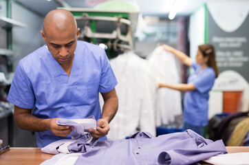 Portrait of man laundry worker checking clean clothes at dry-cleaning facility