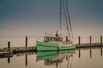 A 1945 converted KHE Army Boat moored at a pier on a cloudy morning with calm waters reflecting the...