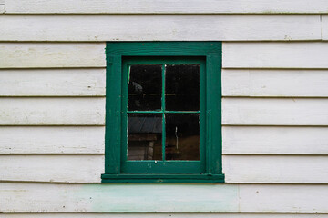 And old window and windows frame painted in green on a building with white siding.