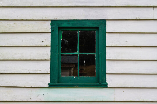 And old window and windows frame painted in green on a building with white siding.