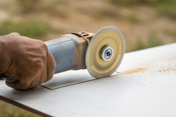 Image of worker using tool to cut tile with dust in background.