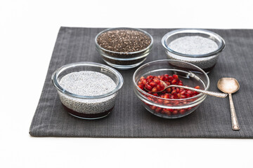 Chia seeds in a glass bowl, Chia seed pudding, and pomegranate seeds close up on white kitchen table