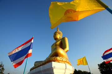 Golden buddha statue with a thai flag and a buddhist flag in during the evening