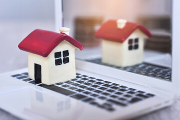 Red roof house on the white laptop with the reflection of house and coins on the laptopn cover background