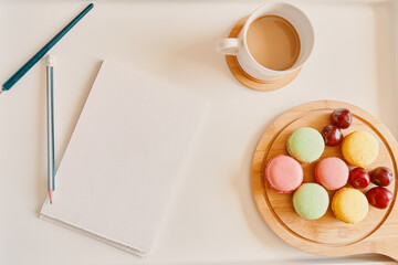 Empty notebook with cup of coffee and dessert on table. White sheet for plans and lists and pencil. Wooden board with almond cookies and cherries. Freelancer's breakfast. Flat lay with copy space.