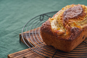Banana bread, cake with banana. Whole loaf on grid. Morning breakfast with tea on green linen textile tablecloth background