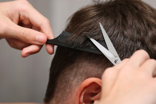 close-up of hands hold scissors and comb while cutting a man's hair. Barbershop. The brown hair is short.