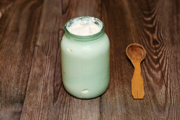 homemade milk sour cream in a glass jar with a rustic wooden spoon. The village produces an agricultural product from milk. Delicious organic food.