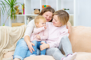 Fototapeta premium Happy daughter and smiling gay mothers in family home. Gay lesbian couple at home. Lesbian couple concept