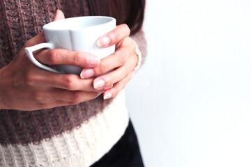 Woman's hands in sweater holding cup of coffee.