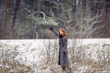Winter landscape with snowfall. A girl in a gray coat is broadcasting something to a small tree.