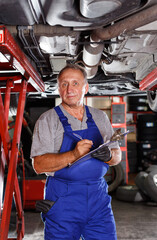 Professional auto mechanic recording list of works on car repair in auto workshop ..