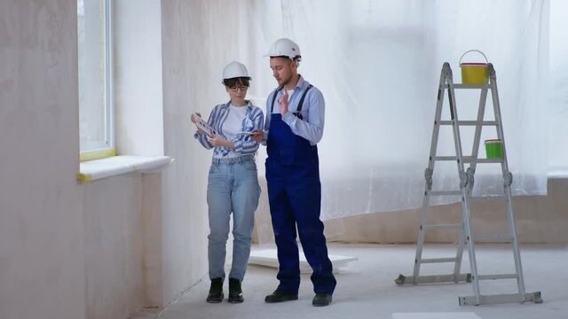 professional male and female builders in safety helmets choose new wall designs from color palette during renovations in an apartment