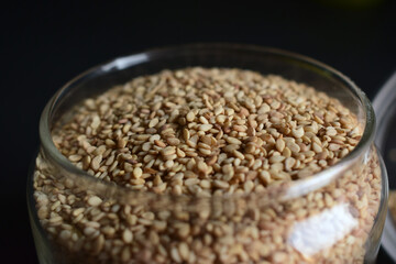 Sesame Seeds in a Open Transparent Glass jar Top View Closeup  On isolated Black Background