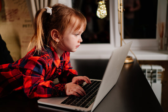 a little girl imitates her mother and works on a computer at home in evening. 