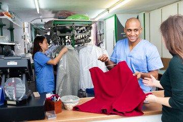 Smiling man drycleaner giving clean garments to client, satisfied with quality