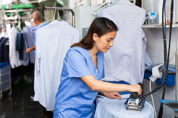 Focused woman laundry worker ironing shirt at dry-cleaning store
