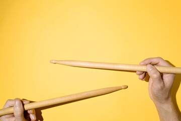 Male hands holding drum sticks, top view yellow background. Drummer
