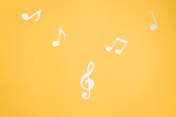 Musical notes and treble clef cut from paper, flat lay yellow background. Music layout top view.