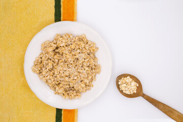 Oatmeal in a plate. Wooden spoon. Colored tablecloth.