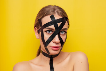 Portrait of a girl in bdsm style in duct tape, fashion, cosmetology, on a yellow background