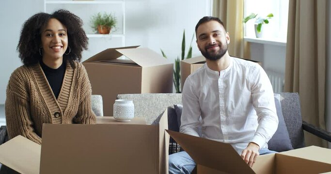 Multi-ethnic couple young novice family young homeowners newlyweds take out boxes take things out of cardboard parcels move to their own home give five with hands, great team work, successful deal