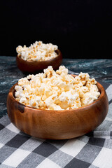 Salt popcorn on dark background. Popcorn in a wooden bowl. Watching a movie with popcorn. vertical photo