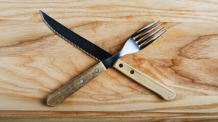 knife and fork stacked in cross on light wood board, top view, banner concept, close-up