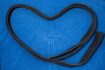 The view from the top. The belt is folded in the form of a heart. Love of judo. Kimono for judo classes and a black belt. The kimono is blue. Background, texture.