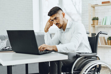 Serious concentrated man in wheelchair using his laptop for work seeking a job in internet