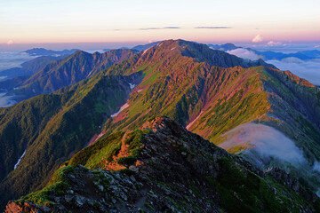 南アルプス　北岳の山頂から　朝日が差し込み朝焼けする間ノ岳方面の稜線を眺める